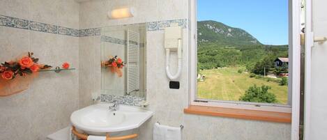 Un baño con un lavamanos grande, un espejo y una ventana que ofrece vistas a un paisaje verde.