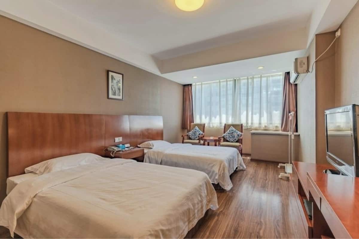 Una habitación de hotel con dos camas, un cabecero de madera, un televisor y una ventana con cortinas.