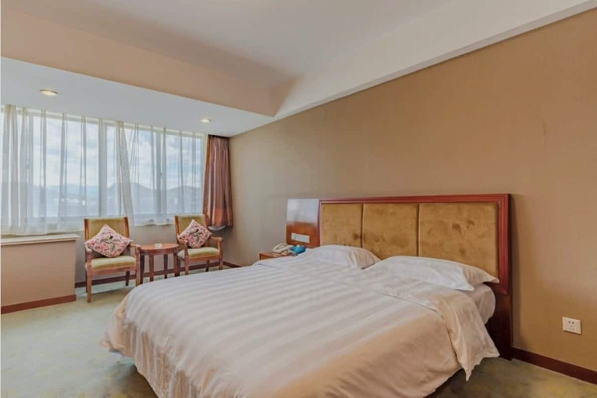Habitación de hotel con una cama grande, dos sillones, una mesita de noche y un ventanal con cortinas.