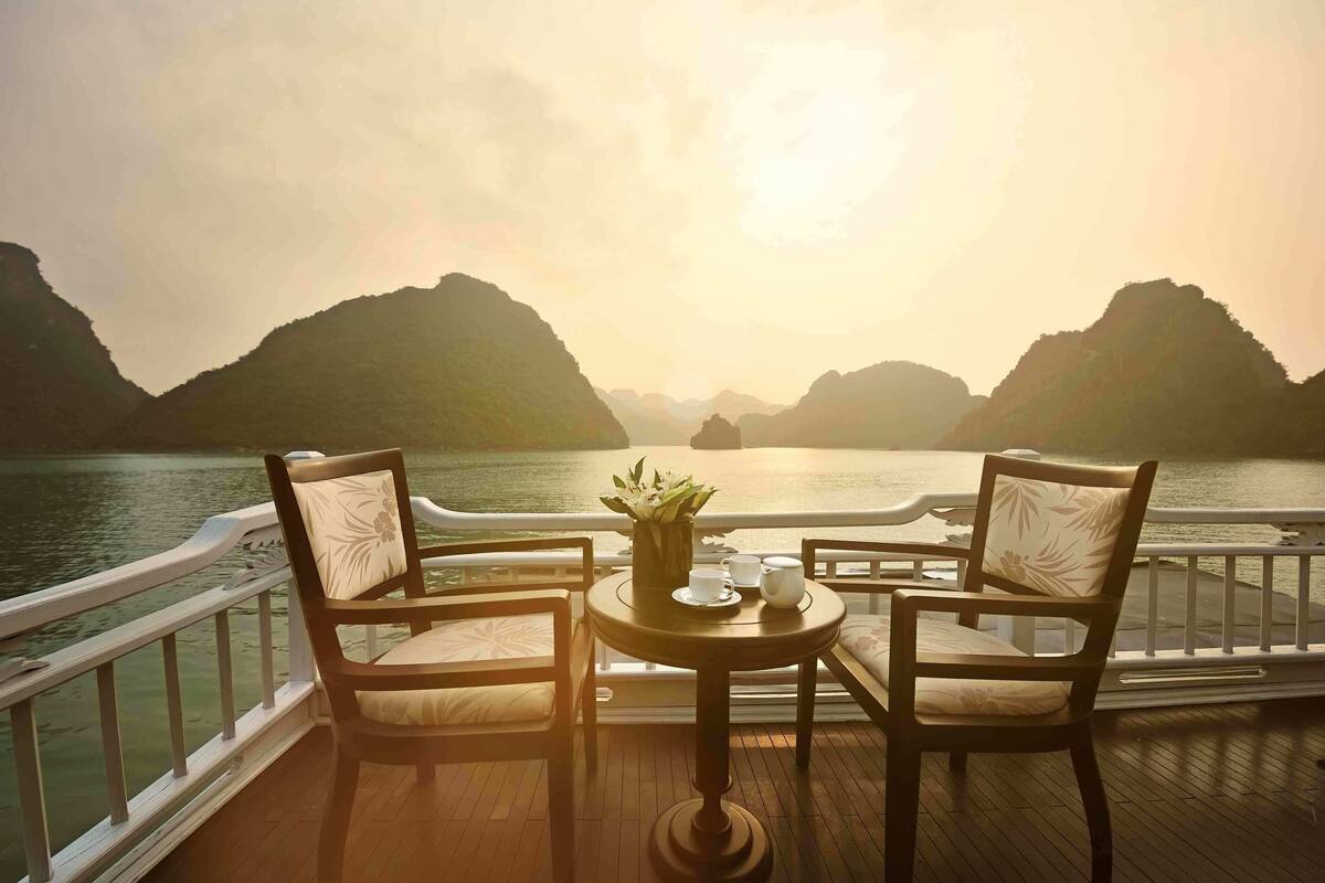 A deck with two chairs and a table, overlooking a body of water and mountains.