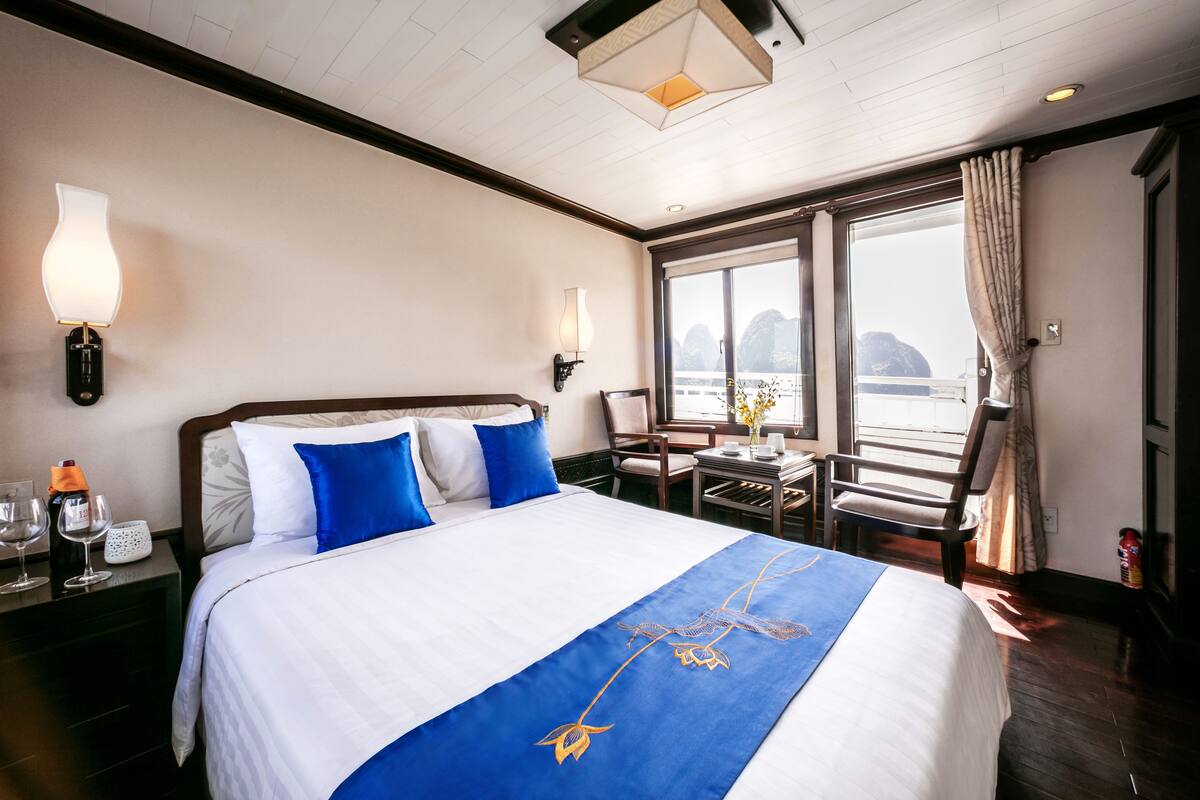 A hotel room with a large bed, two bedside tables, a chair, a small table, and a window with curtains.