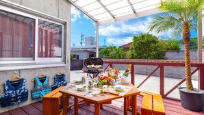 Un espacio comedor al aire libre con techo, una parrilla, mesas y sillas de madera.