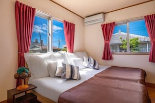 Un dormitorio con cama, almohadas, una mesita de noche y una ventana con cortinas.