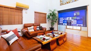 Sala de estar con un sofá de cuero marrón, una mesa de comedor de madera para cuatro personas y un televisor de pantalla plana mostrando servicios de streaming.