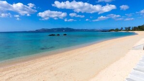 A beach with clear turquoise water, a sandy shore, and a distant mountain range under a blue sky with scattered clouds. - Private Vacation Home COZY (Nago)