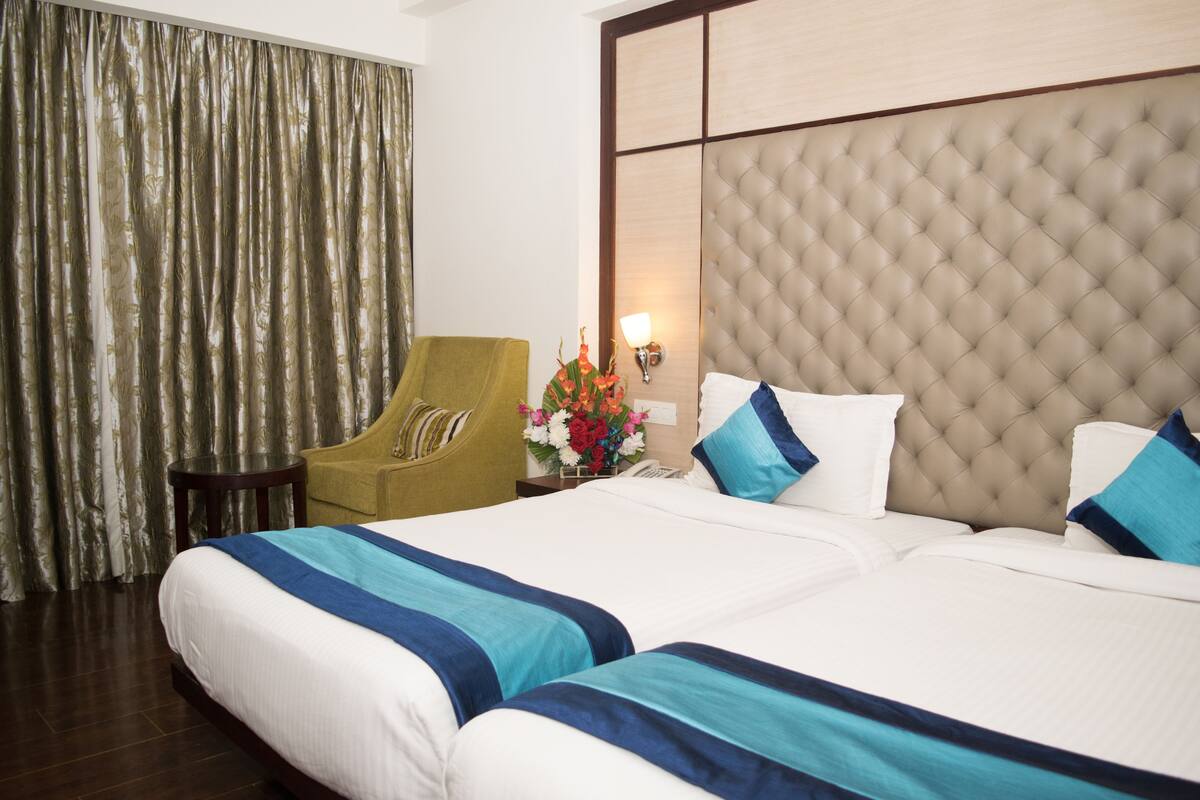 A hotel room with a large bed, a green armchair, a small table, and a decorative vase with flowers.