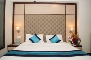 A hotel room with a large bed, two nightstands, a wall-mounted lamp, a floral arrangement, and a window. - Hotel Mint Oodles (New Delhi)