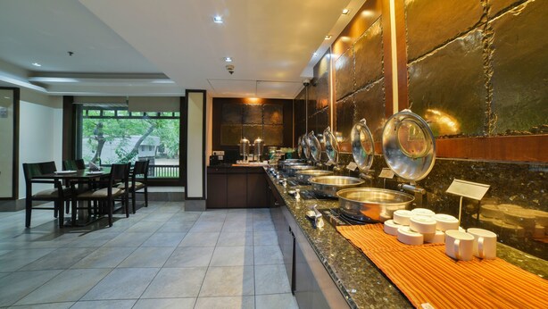 A buffet area with a long counter, multiple serving stations, and a seating area with tables and chairs. - Hotel Mint Oodles (New Delhi)