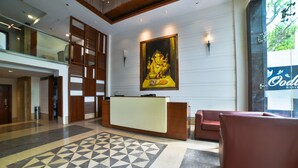 A reception area with a geometric patterned floor, a reception desk, a large framed artwork, and a seating area with a view of the outdoors. - Hotel Mint Oodles (New Delhi)