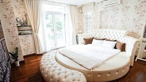 A bedroom with a large bed, a round ottoman, and floral wallpaper. - 5 Bedrooms Pool Villa w Karaoke (Ho Chi Minh City)