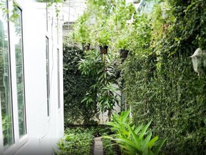 Un sendero estrecho y cercado, flanqueado por abundante follaje, que conduce a la entrada de un edificio blanco.