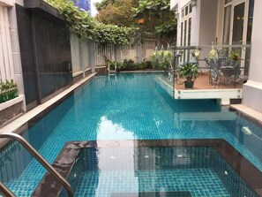 Una piscina con agua azul cristalina, rodeada por un solárium con baldosas y una barandilla metálica.