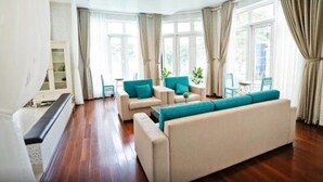 A spacious living room with a large beige sofa, two armchairs, a coffee table, and a chandelier. Large windows with curtains allow natural light to fill the room. - 5 Bedrooms Pool Villa w Karaoke (Ho Chi Minh City)