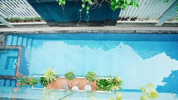 A pool with clear blue water, surrounded by plants and a wooden wall. - 5 Bedrooms Pool Villa w Karaoke (Ho Chi Minh City)