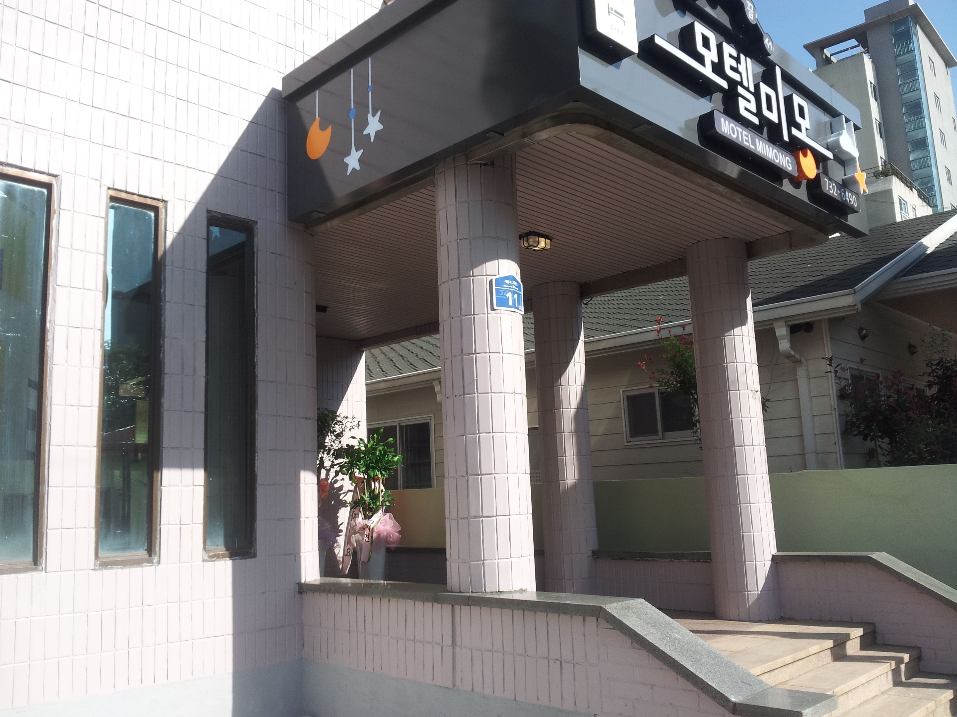 A building with a sign for 'Motel Mimong' and a number '11' on a pillar.