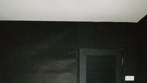 Una habitación con una puerta de color oscuro, piso a cuadros y una cama blanca al frente.