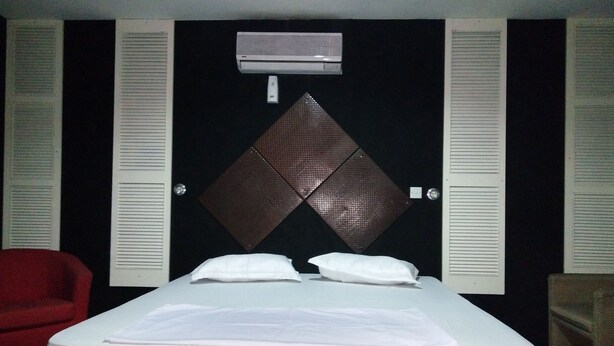 Habitación de hotel con una cama, una silla roja y un aire acondicionado de pared.