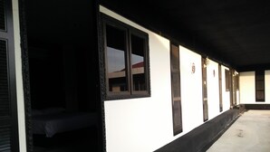Un pasillo con una cama en una de las habitaciones, una pared blanca con detalles negros y un toldo negro sobre la entrada.