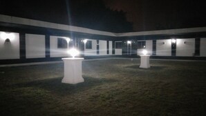 Un patio exterior con dos mesas blancas y un edificio con varias ventanas al fondo.