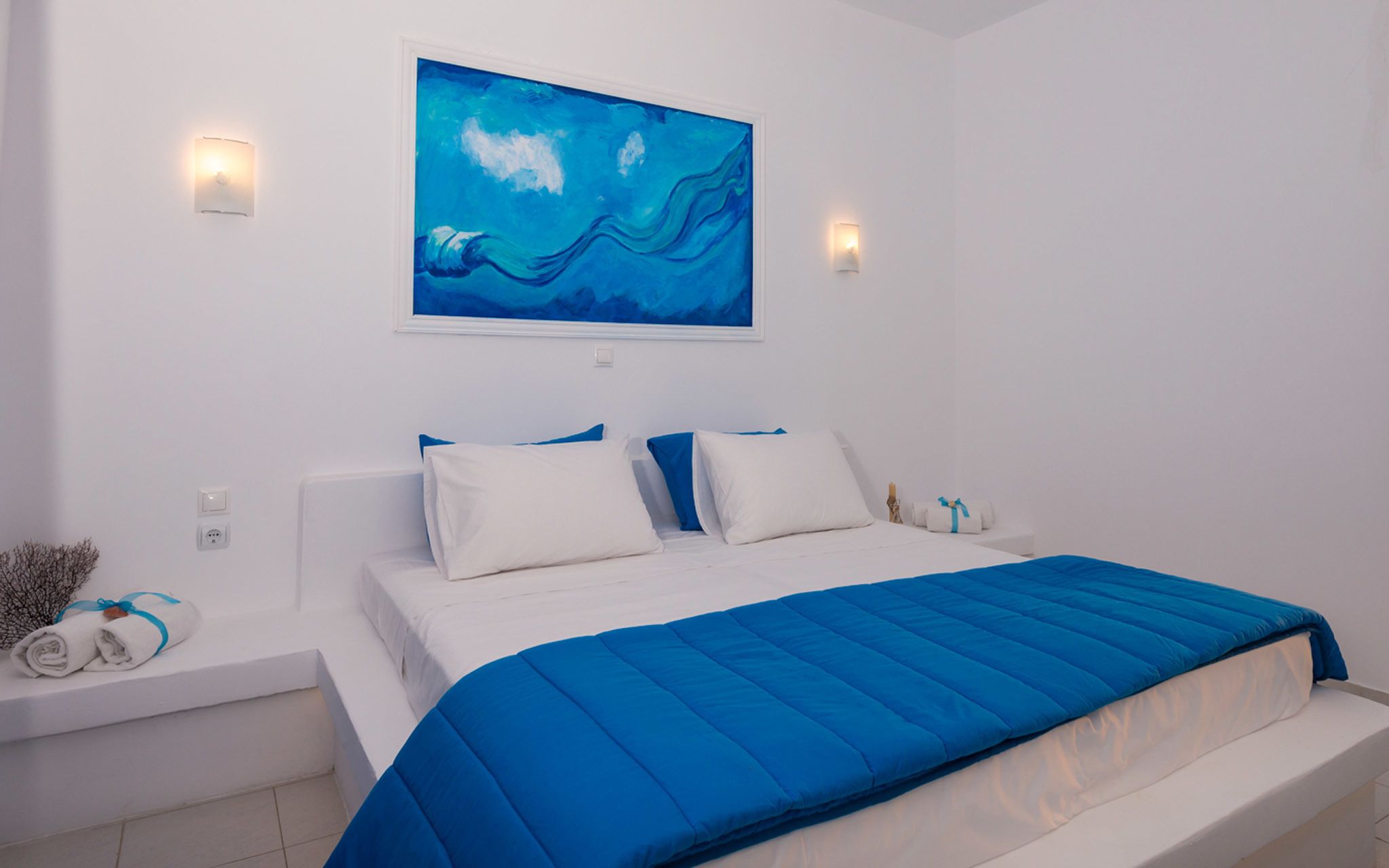 Ein modernes Schlafzimmer mit einem Bett, weißen Wänden und einem blauen Bild darüber.