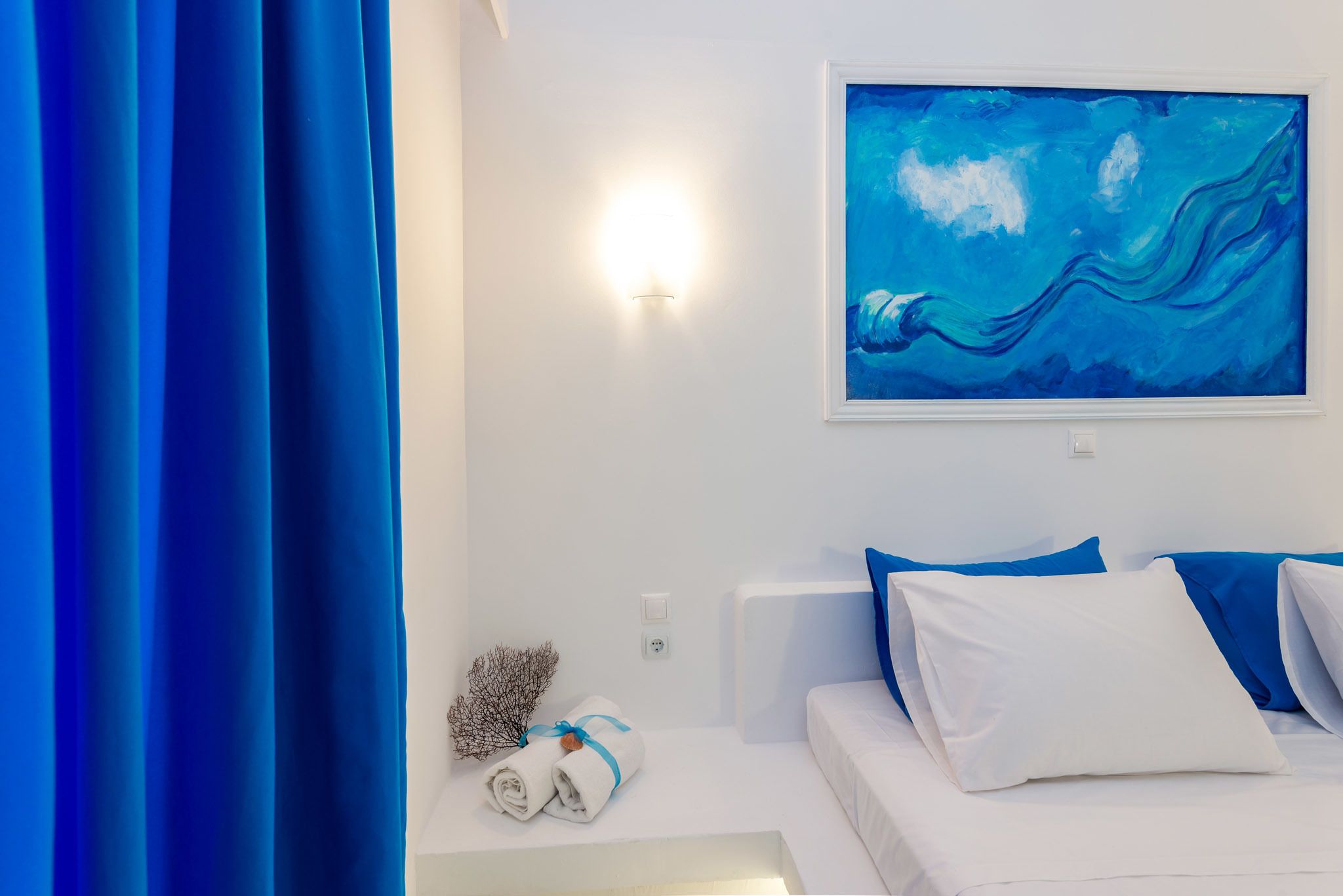 A modern hotel room with a bed, a painting, and a wall-mounted light.