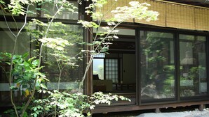 Un edificio japonés tradicional con amplios ventanales de vidrio, fachada de madera y un jardín con rocas y plantas.