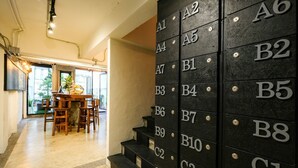 Un vestíbulo de hotel con una escalera que da a habitaciones numeradas, una mesa de madera con sillas y vistas al exterior.