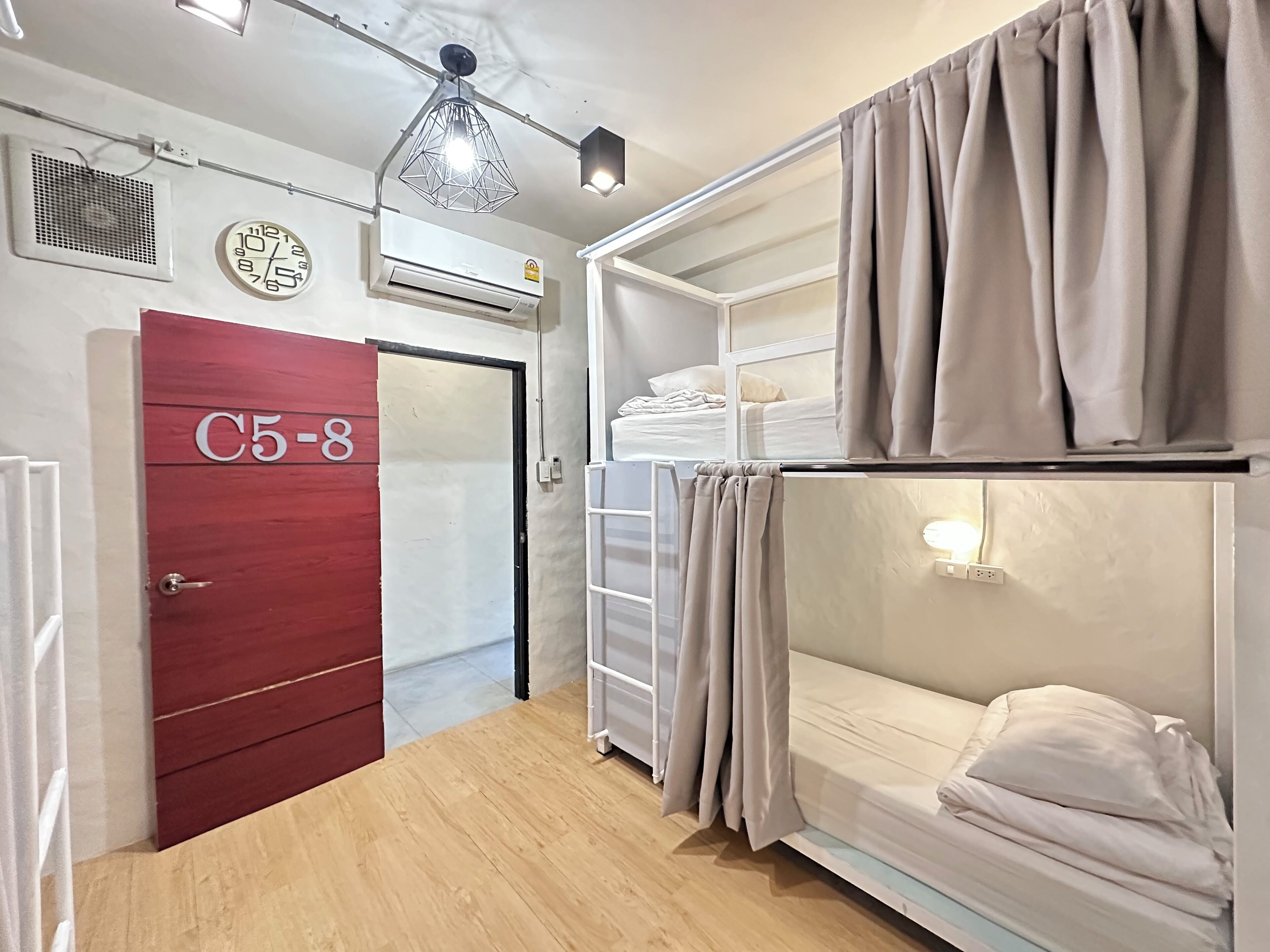 A dormitory room with bunk beds, a wardrobe, an air conditioning unit, a clock, and a hanging light fixture.
