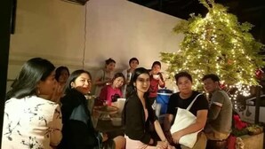 Un grupo de personas reunidas alrededor de un árbol de Navidad decorado en una habitación con una distribución sencilla y funcional.