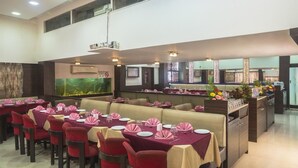 Un restaurante con varias mesas dispuestas, servilletas rosas y sillas rojas, un acuario grande y una zona de bar con flores.