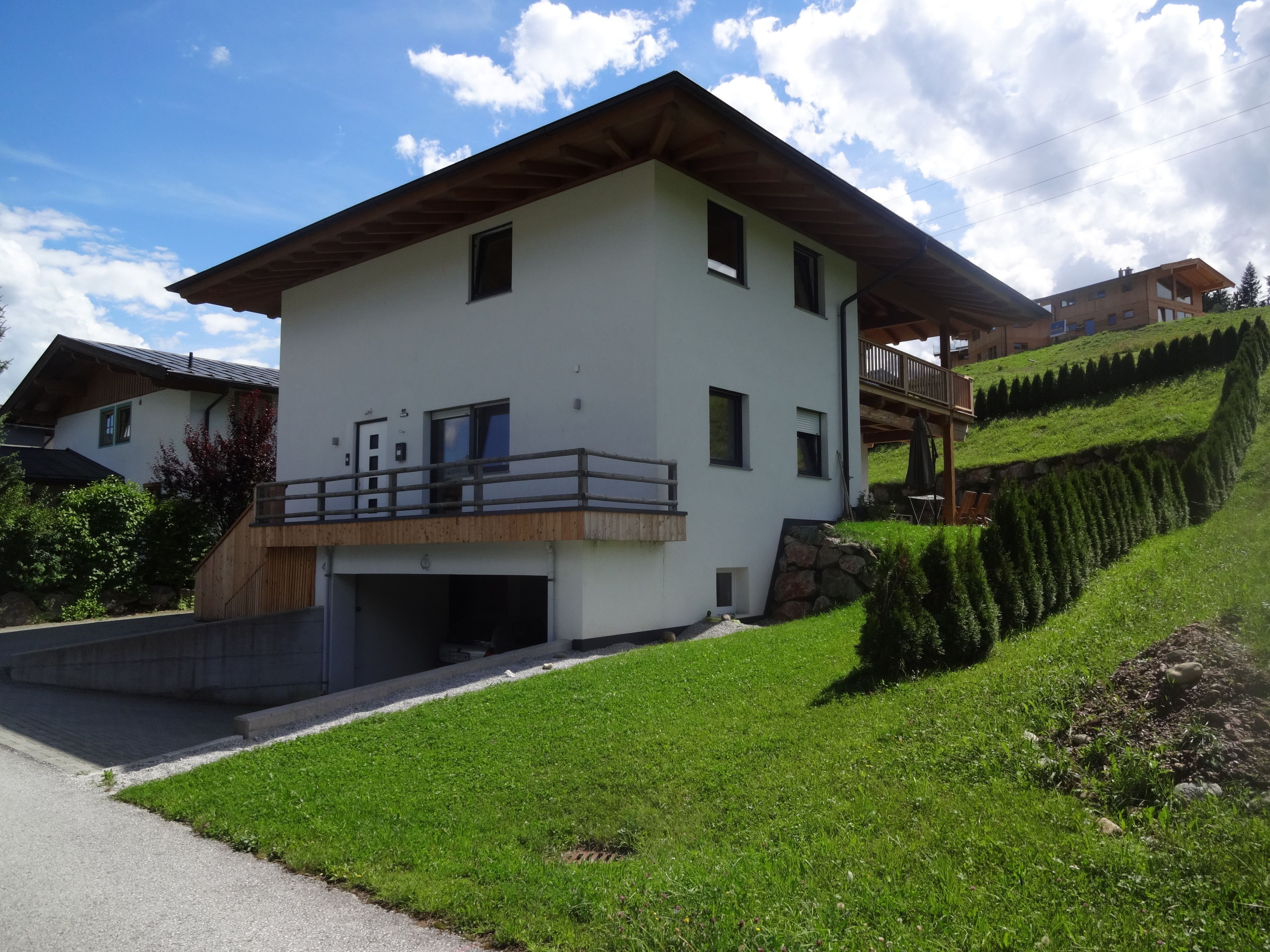 A modern two-story house with a flat roof, a balcony, and a stone foundation.