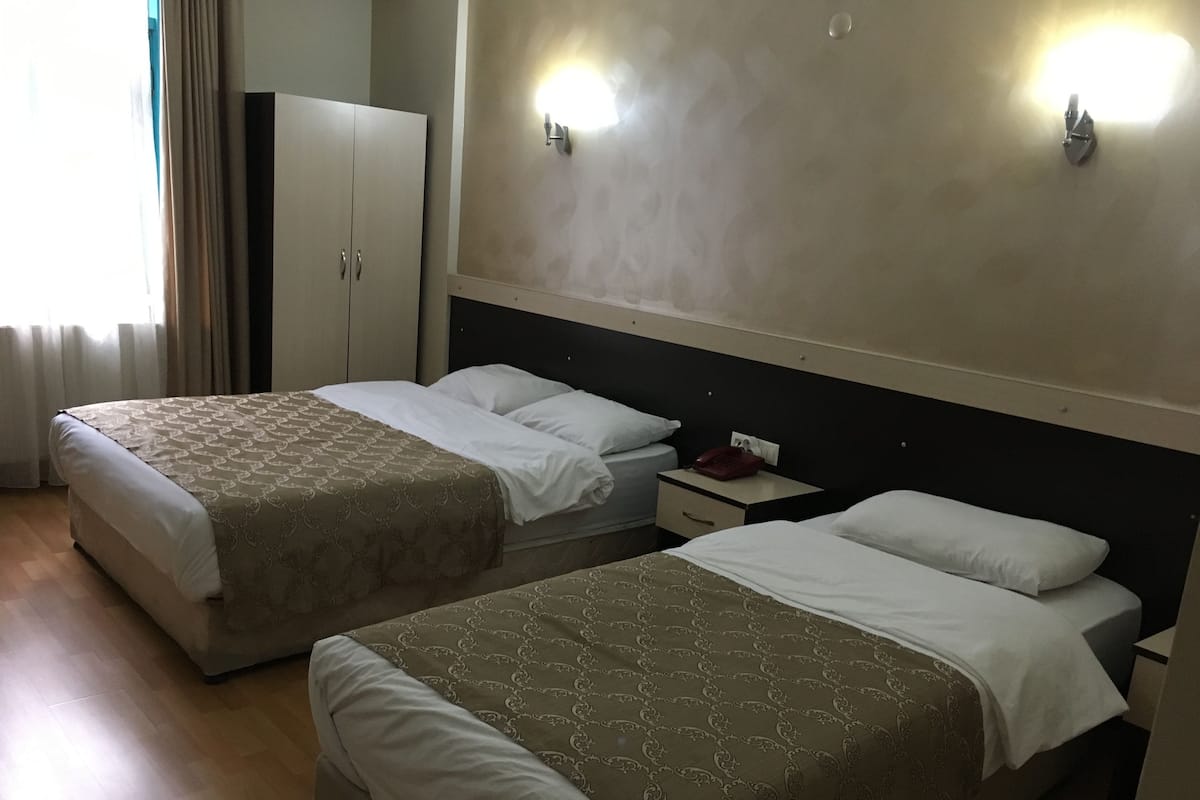 A hotel room with two beds, a wardrobe, a bedside table with a phone, and a wall-mounted light fixture.