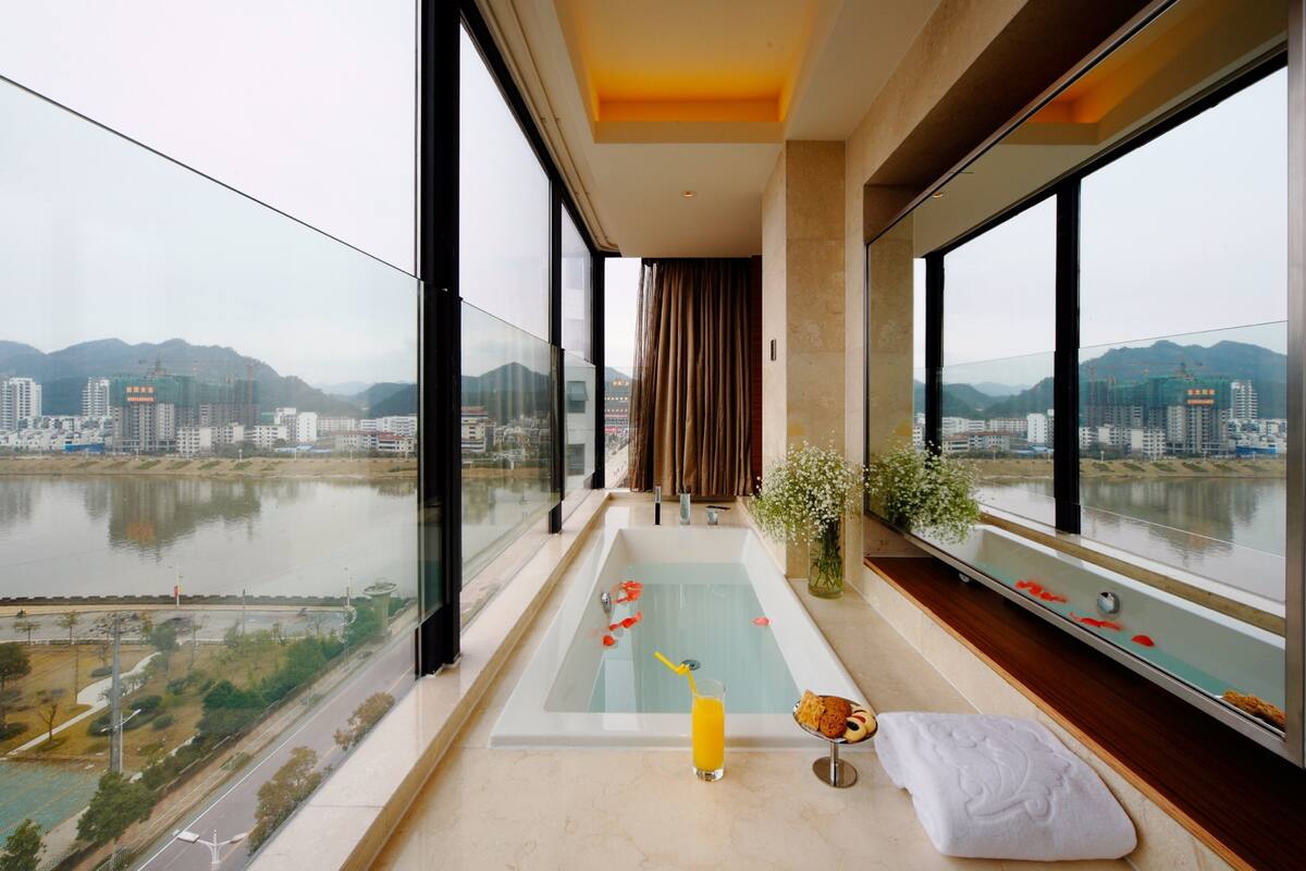 Ein modernes Badezimmer mit einer großen Badewanne, einer Duschkabine aus Glas und Blick auf Stadt und Fluss.