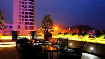 An outdoor seating area with tables and chairs, a potted plant, and a building in the background.