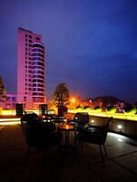 An outdoor seating area with tables and chairs, a potted plant, and a building in the background.