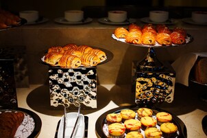 Un bufé con pastelería y productos de panadería, incluyendo croissants y muffins, dispuestos en elegantes soportes.