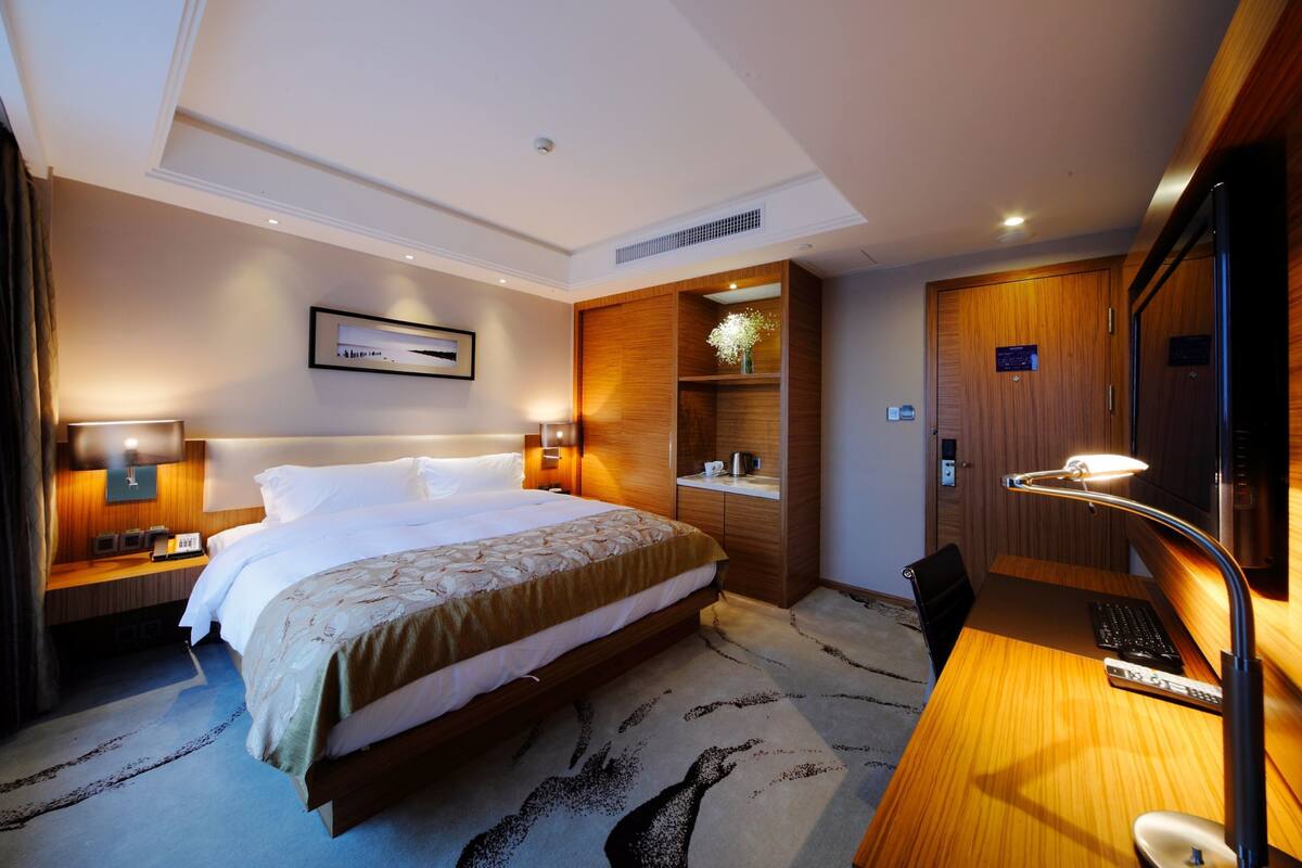 Ein Hotelzimmer mit einem großen Bett, Nachttischen mit Lampen, einem Schreibtisch mit Computer und einem Holzschrank.