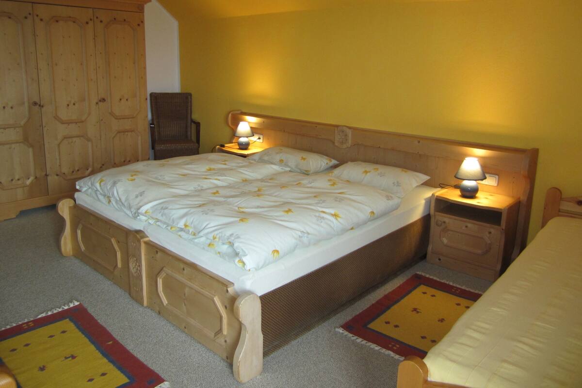Een slaapkamer met een groot bed, twee nachtkastjes met lampen, een houten kledingkast en een stoel.