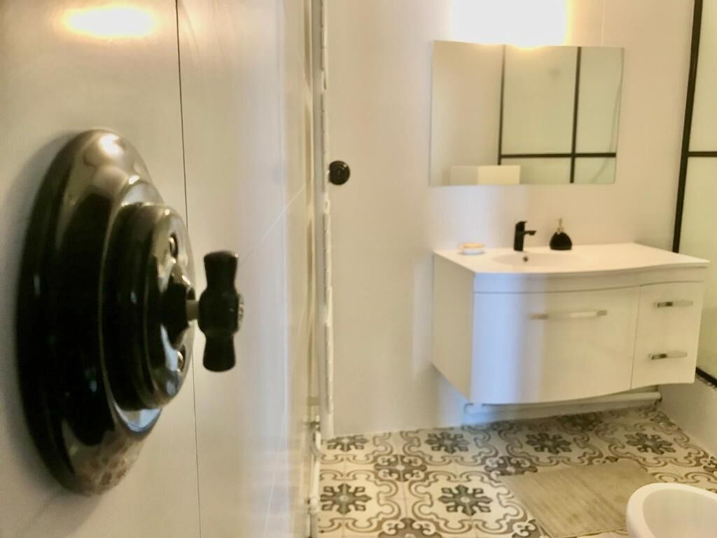 Une salle de bain avec un lavabo blanc, un miroir et des carreaux de sol à motifs.