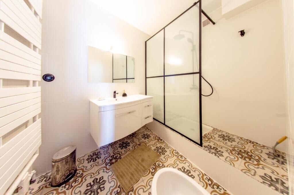 A bathroom with a white sink, mirror, and shower. The floor has patterned tiles.