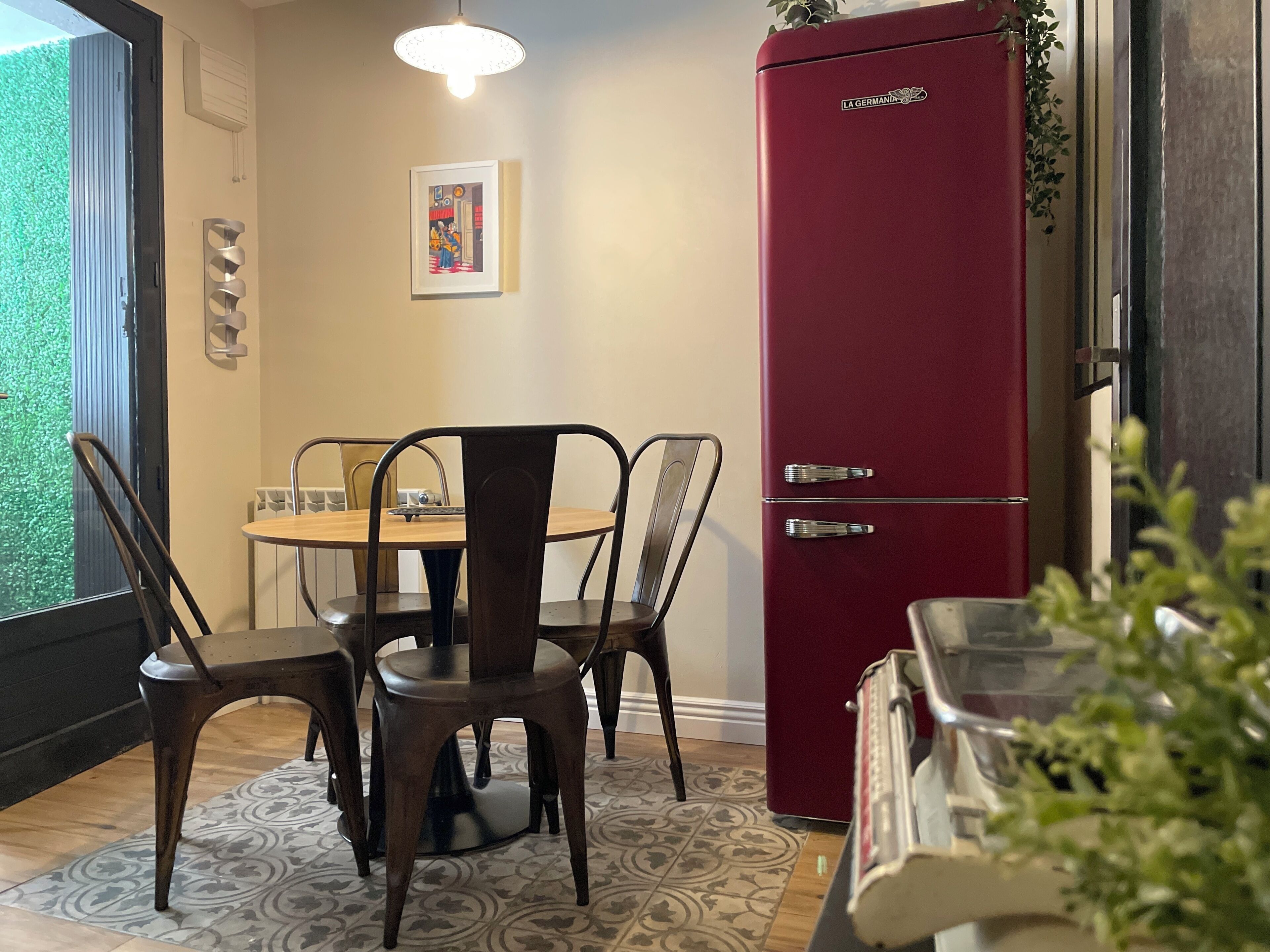 A dining area with a table, chairs, a red refrigerator, and a wall-mounted picture.