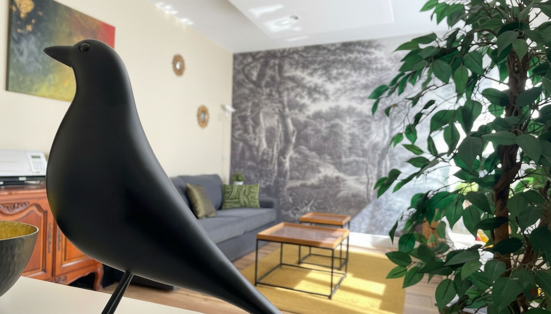 A modern living room with a black bird sculpture, a grey sofa, a small table, and a plant.