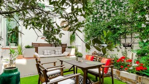 A patio area with a wooden table and chairs, a sofa, and a variety of plants and flowers. - Le Rétro Mirabeau - Maison de Famille (Narbonne)