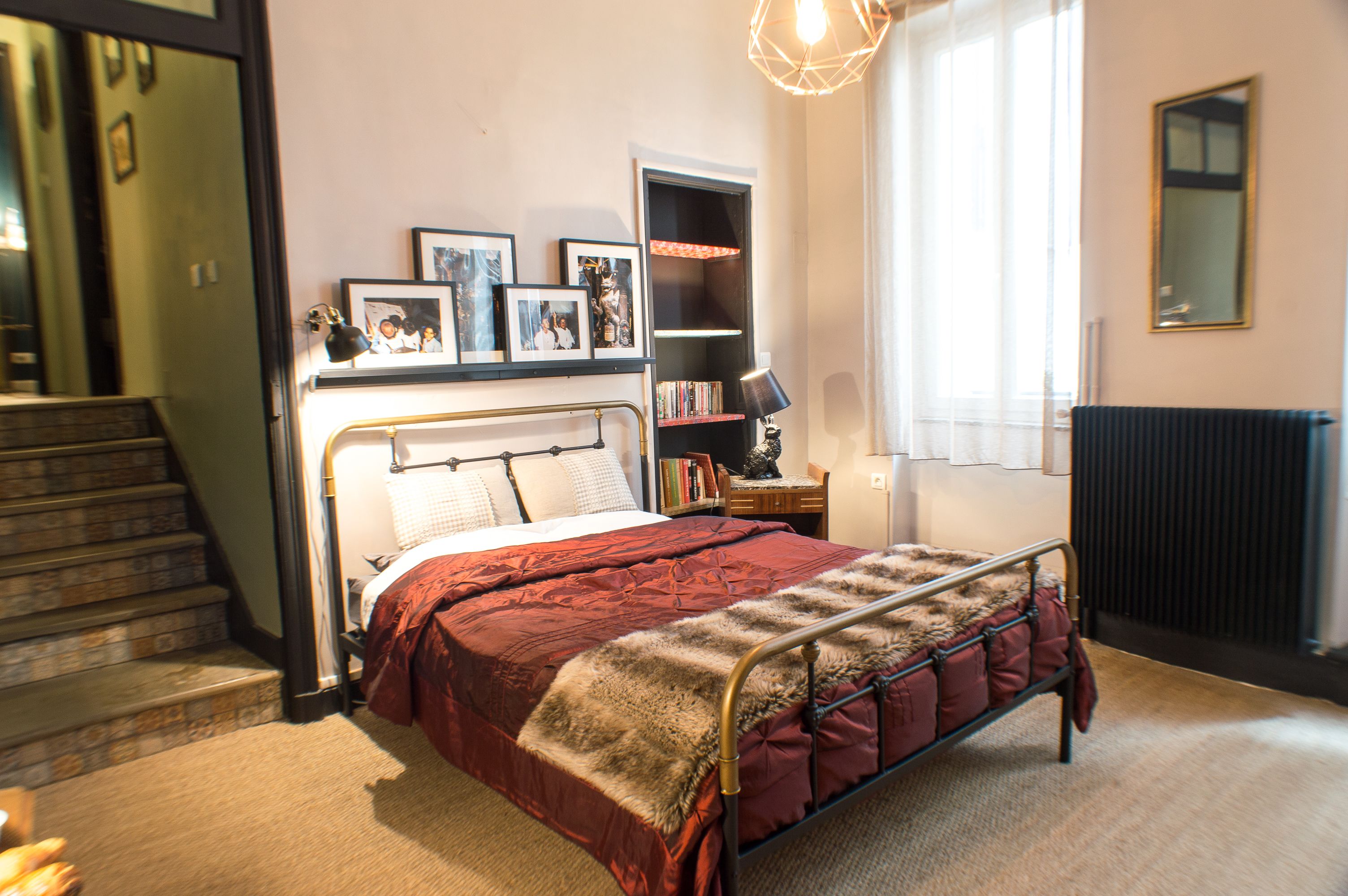 A bedroom with a bed, a bookshelf, a radiator, and a staircase.
