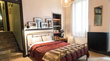 A bedroom with a bed, a bookshelf, a radiator, and a staircase.