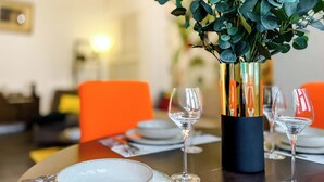 A dining table with a vase of green foliage, clear wine glasses, and orange chairs. - Le Rétro Mirabeau - Maison de Famille (Narbonne)