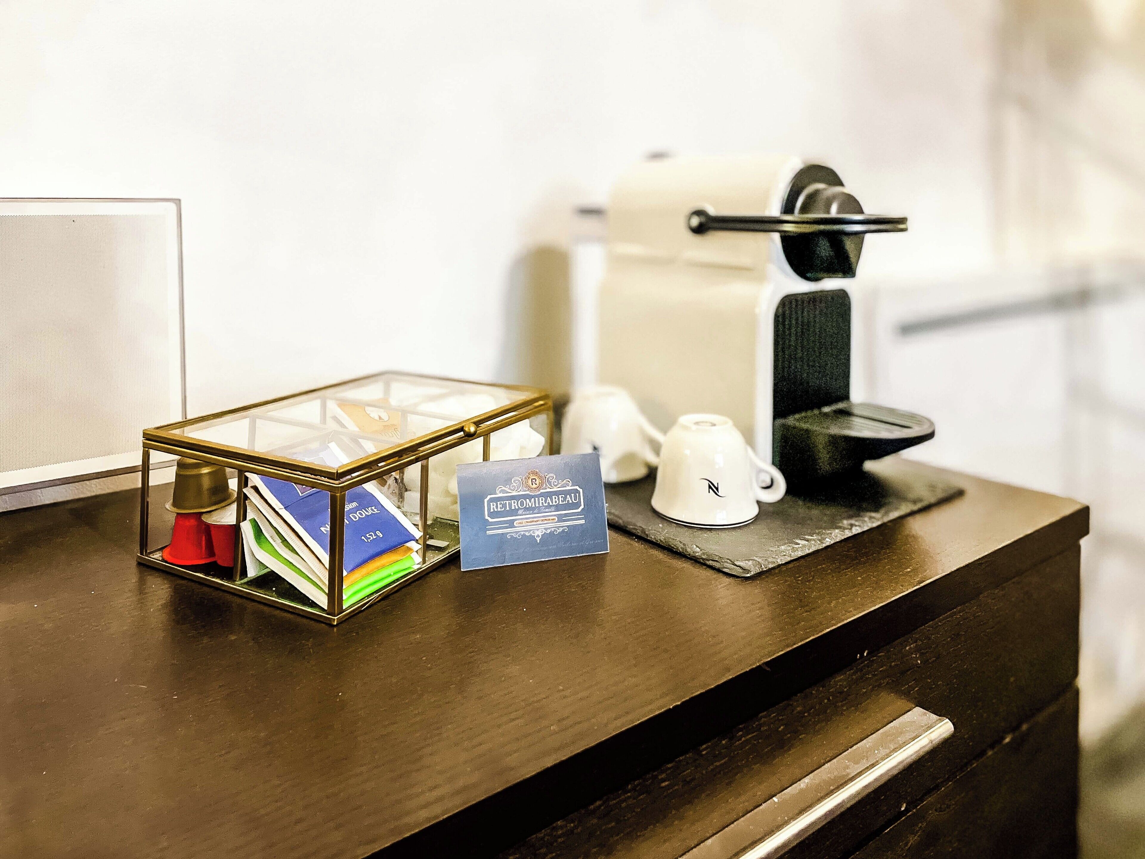 A hotel room counter with a glass display case containing toiletries, a coffee machine, and a card.