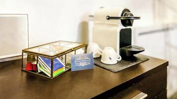 A hotel room counter with a glass display case containing toiletries, a coffee machine, and a card.
