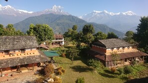 A rural village with traditional houses, a green field, and a mountain range in the background. - Mystique Highland Resort (Pokhara)