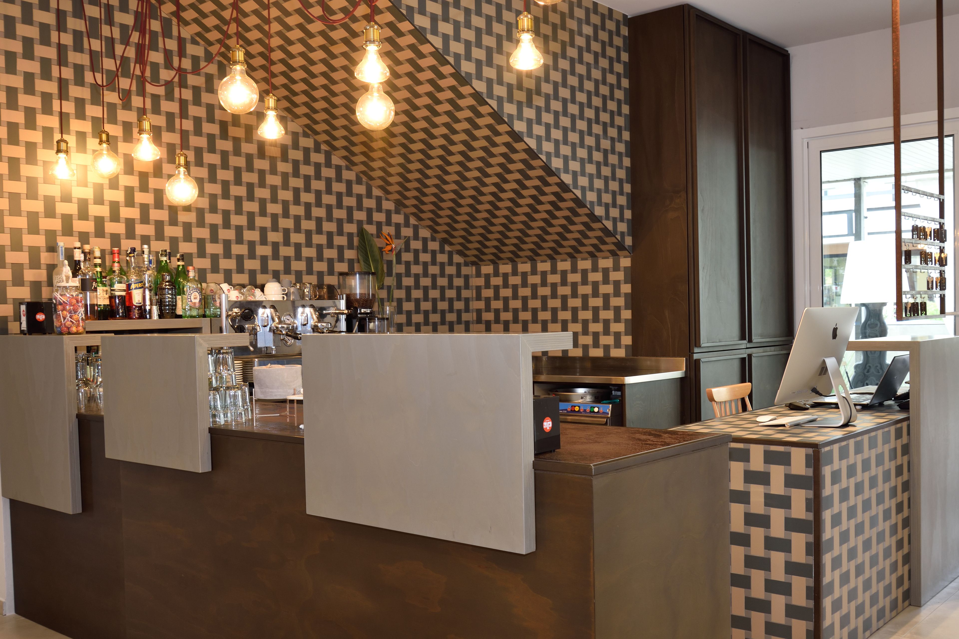 A modern bar area with a checkered tile wall, a bar counter, and a seating area with a laptop and a chair.